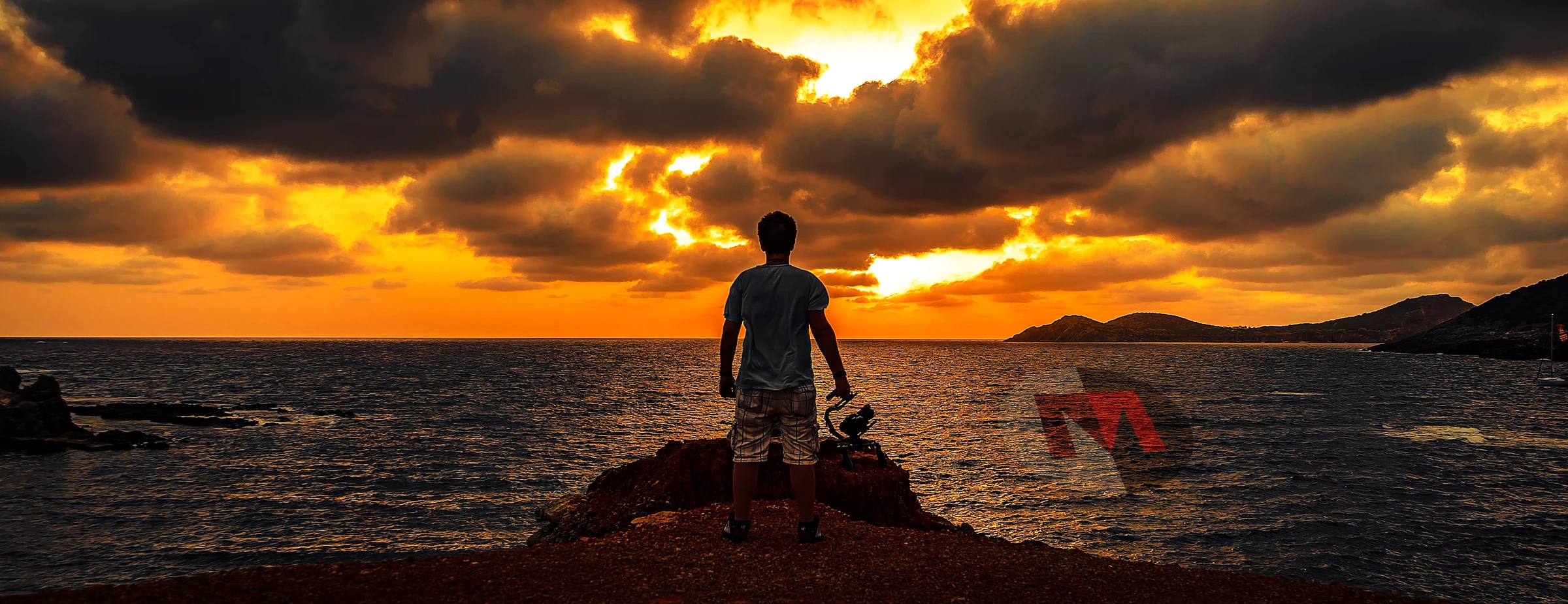 Kameramann am Meer vor einem leuchtenden Sonnenuntergang